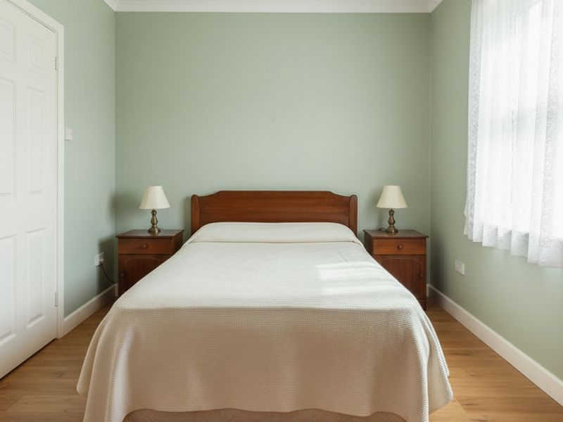 The same bedroom with soft sage green walls and a pale oak floor. The bed, both bedside tables and both lamps are unchanged and in the same positions.
